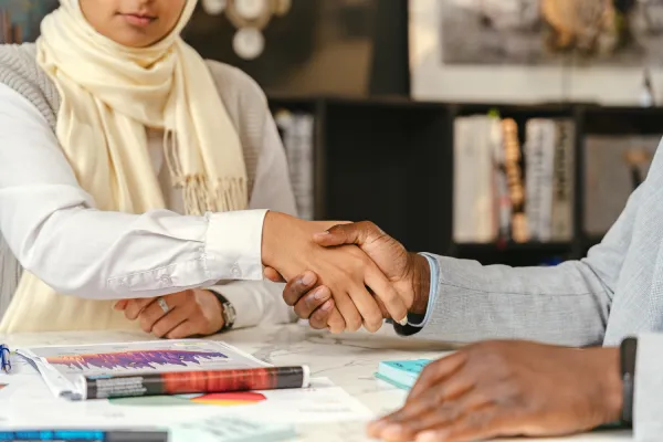 Two people shaking hands over a desk with paperwork